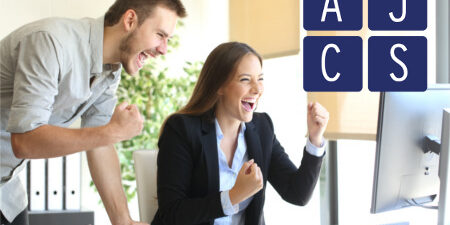 Excited businesspeople online Glückliche Mitarbeiter jubeln vor einem Computer, im Vordergrund sieht man das Logo der AJCS GmbH