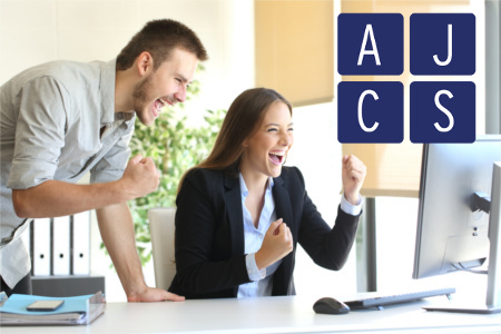 Glückliche Mitarbeiter jubeln vor einem Computer, im Vordergrund sieht man das Logo der AJCS GmbH