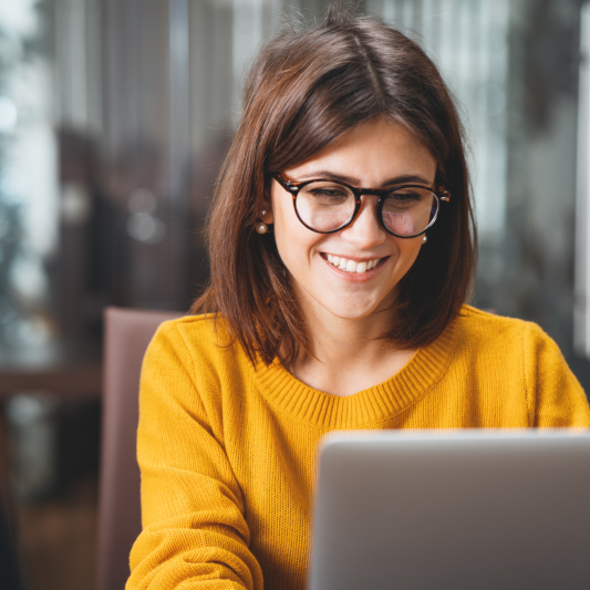 Businessfrau in gelbem Pullover arbeitet glücklich am Laptop