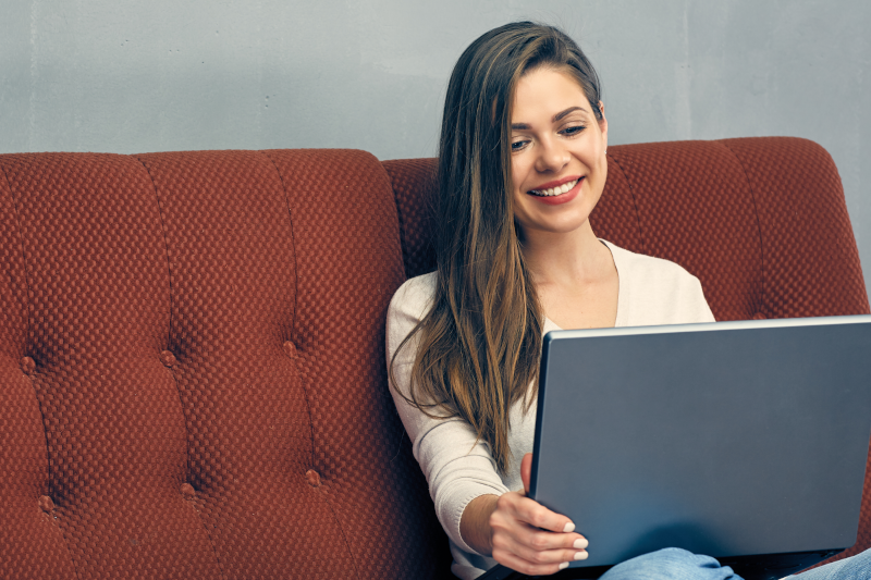 Glückliche Businessfrau auf rotem Sofa mit Laptop