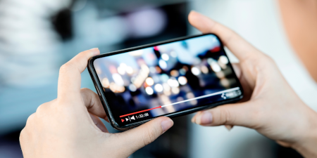 Hände die ein Smartphone in der Hand halten auf dem ein Video läuft